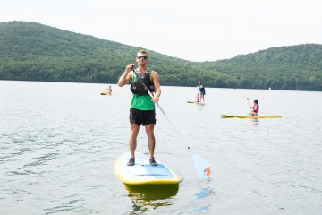 a person paddleboarding on a reservoir with kayaks in the background