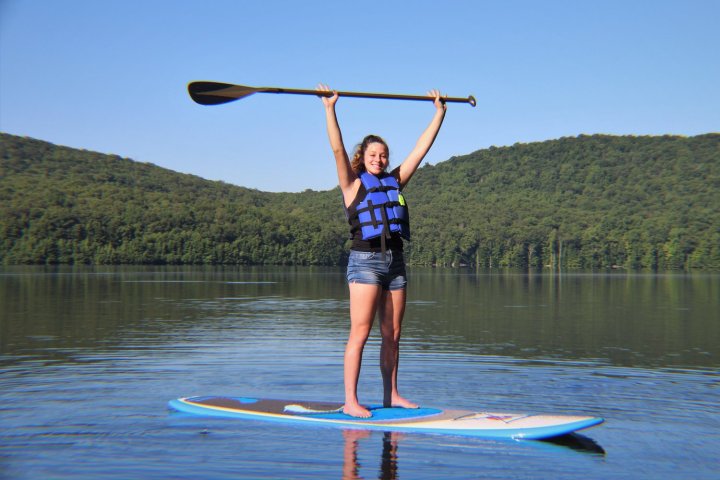 Stand Up Paddleboarder on Monksville Reservoir holds the paddle above her head