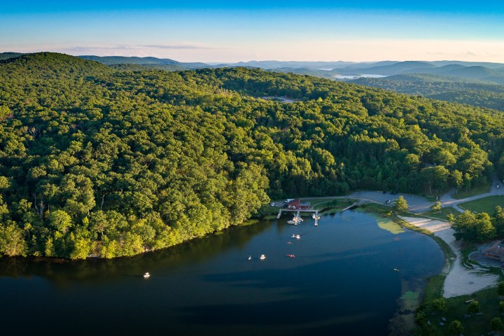 an aerial photo of a tree covered hillside next to a body of water
